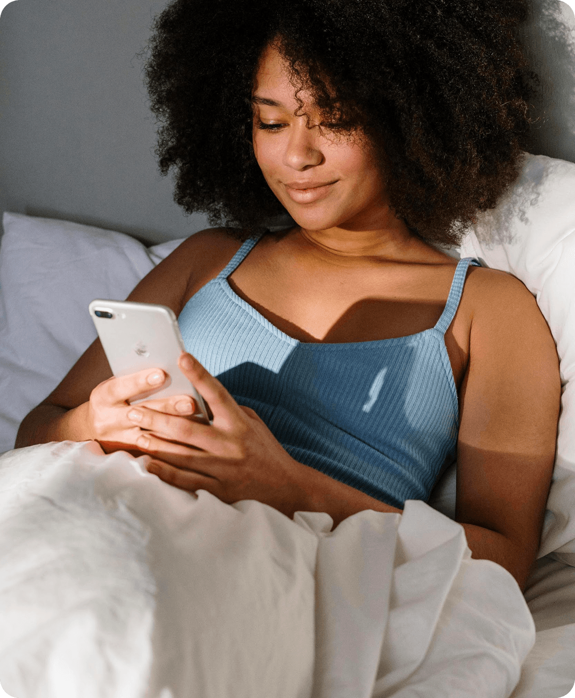 Junge Frau im Bett mit Smartphone, entspannter Blick auf die Finanzen